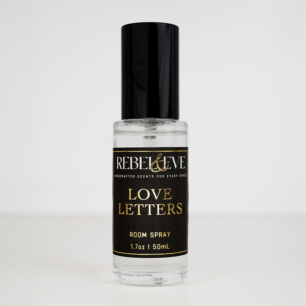 A bottle of 'Love Letters' room spray with a black cap and a label that includes the product name and the scent, peony, written in a stylish font.