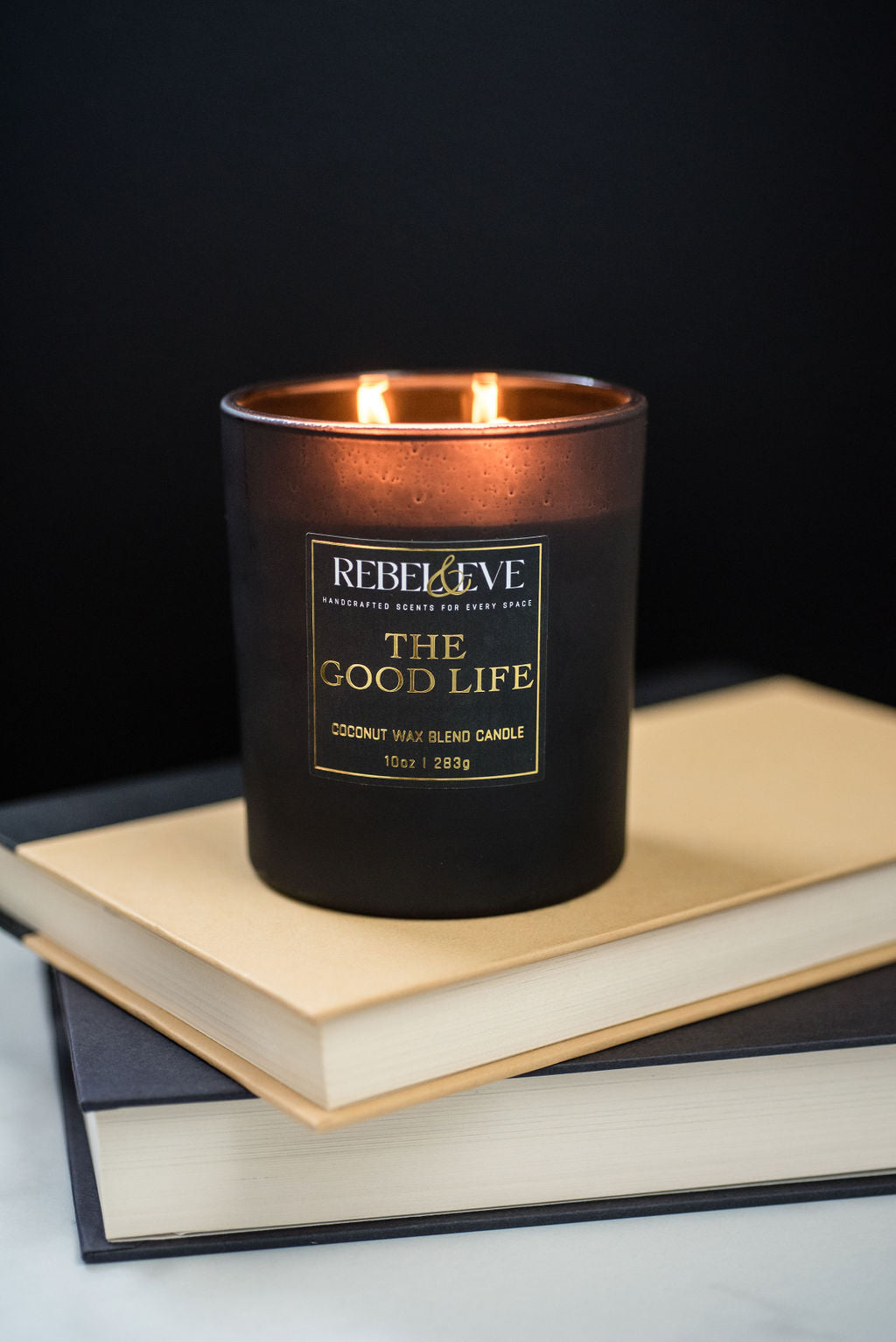 A matte black candle with the text Rebel and Eve and The Good Life on it. 