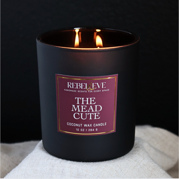 Black The Mead Cute candle with a purple label on a white surface